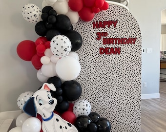 May include: A festive party decoration featuring a Dalmatian theme. A large balloon garland in red, black, and white, with paw print balloons, surrounds a backdrop with the text "Happy 3rd Birthday Dean". A Dalmatian cutout is at the base.
