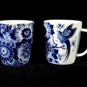 Könnte beinhalten: Drei weiße Keramikbecher mit blauen Blumen- und Vogelmotiven. Zwei Becher haben Henkel, der mittlere Becher ist zylindrisch. Die blauen Designs umfassen Blumen und Vögel auf weißem Hintergrund.