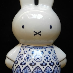 May include: White ceramic bunny figurine with blue and white patterned clothing. The bunny has long ears and a simple face.