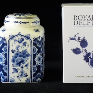 May include: A white ceramic jar with a blue and white floral design. The jar has a lid and is in a box with the words "Royal Delft 1653 Koninklijke Porceleijne Fles Original Delft Blue" printed on it.