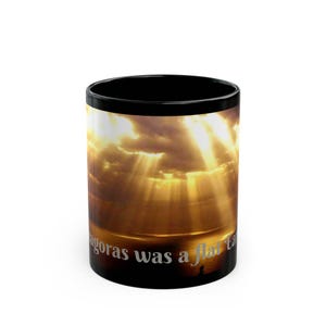 Puede incluir: Taza de café negra con un diseño envolvente que presenta un cielo dramático con luz solar dorada que atraviesa las nubes. El texto "agoras was a flat ta" está impreso en la taza.