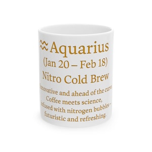 May include: White ceramic mug with gold text. The mug features the Aquarius zodiac symbol and the text "Aquarius (Jan 20 - Feb 18) Nitro Cold Brew." Additional text describes the coffee as innovative and futuristic.