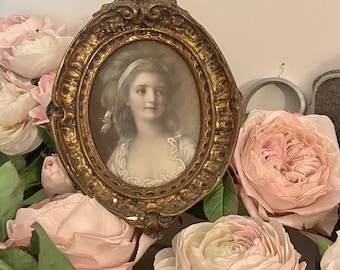 Puede incluir: Un retrato ovalado antiguo en un marco dorado ornamentado. El retrato representa a una mujer con un pañuelo blanco. El marco está rodeado de suaves rosas rosas y hojas verdes, creando una estética romántica y vintage.