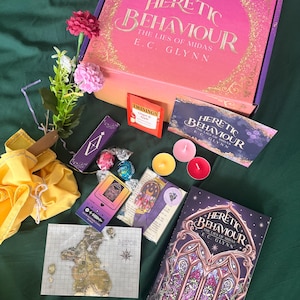 May include: An assortment of items including a book and box titled "Heretic Behaviour: The Lies of Midas" by E.C. Glynn, tea, candles, and a map. The color palette features purple, pink, and gold accents.
