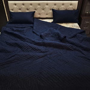 May include: A navy blue quilted bedspread with a diamond pattern. The bedspread is folded back on a bed with two pillows.