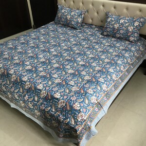 Könnte beinhalten: Ein blauer Bettbezug mit einem Blumenmuster und einem weißen Rand. Der Bettbezug liegt auf einem Bett mit zwei Kissen.
