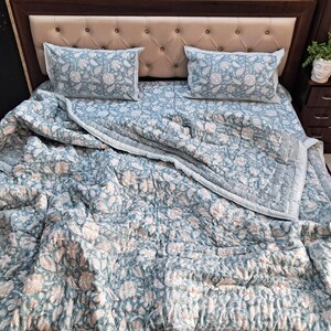 May include: A blue and white floral patterned quilt with a white border. The quilt is folded on a bed with matching pillowcases.