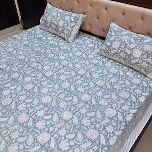 May include: A blue and white floral patterned bed sheet with matching pillowcases. The bed sheet has a white border and the pillowcases have white trim.