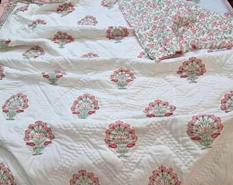 May include: White quilted bedspread with a repeating floral pattern in red and green. The flowers are stylized and arranged in a symmetrical design. The bedspread has a matching pillowcase with a similar floral print.