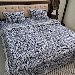 May include: A blue and white floral patterned quilt set on a bed with two matching pillowcases. The quilt is made of cotton and has a quilted design.