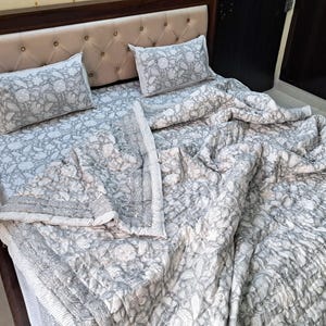 May include: A grey and white patterned bedspread with a white border. The bedspread is made of cotton and is soft and comfortable. The bedspread is perfect for adding a touch of elegance to any bedroom.