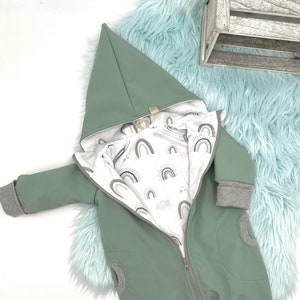 Könnte beinhalten: Hellgrüner Baby-Overall mit Kapuze und durchgehendem Reißverschluss. Das Innenfutter hat einen weißen Stoff mit einem sich wiederholenden Regenbogenmuster. Die Manschetten und der Besatz sind grau. Der Overall ist für Säuglinge und Kleinkinder konzipiert.