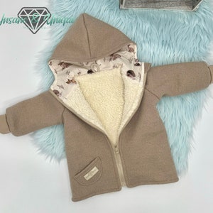 Könnte beinhalten: Eine braune Kapuzenjacke mit Reißverschluss und einer Tasche auf der Vorderseite. Die Jacke ist mit weißem Fleece gefüttert und hat ein süßes Tiermuster, das die Kapuze auskleidet.