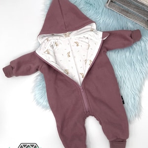 Könnte beinhalten: Ein mauvefarbener Baby-Strampler mit Reißverschluss und Kapuze. Der Strampler hat ein weißes Futter mit einem kleinen Hasenmuster.