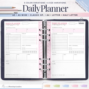 Op de afbeelding: Open dagplanner met roze en witte gestreepte accenten. De planner bevat secties voor prioriteiten, takenlijsten, maaltijdplannen en notities. De planner zit in een donkerblauwe map met zilveren ringen.