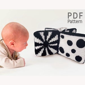 Pode incluir: Brinquedo de crochê preto e branco para bebê com um padrão de sol, bolinhas e listras. O brinquedo é feito de fio macio e é perfeito para bebês explorarem e aprenderem sobre diferentes texturas. Padrão PDF.