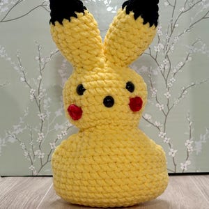 Könnte beinhalten: Ein gelbes, gehäkeltes Plüschtier in Form eines Kaninchens mit schwarzen Ohren und roten Wangen.