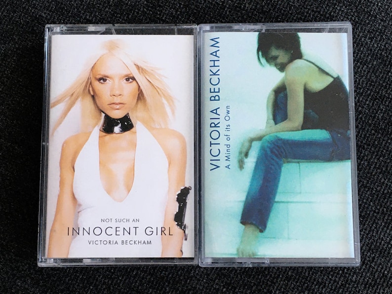 May include: Two cassette tapes featuring Victoria Beckham. One cover shows her in a white halter top with the text "NOT SUCH AN INNOCENT GIRL". The other cover has a photo of her with the text "A Mind of its Own".