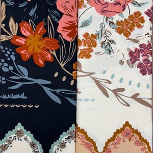 May include: Two fabric rolls with floral designs. One displays large orange and coral flowers on a navy background. The other has pink and brown flowers on a cream background. Both have a scalloped edge.