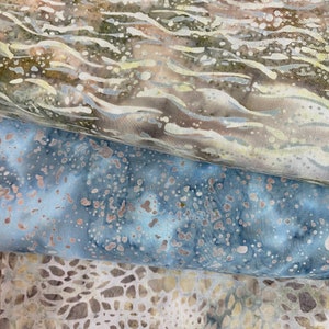 May include: Three pieces of fabric with different patterns. The top piece is a light brown fabric with a wavy pattern. The middle piece is a light blue fabric with a speckled pattern. The bottom piece is a light beige fabric with a geometric pattern.