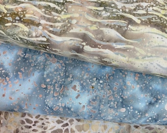 May include: Three pieces of fabric with different patterns. The top piece is a light brown fabric with a wavy pattern. The middle piece is a light blue fabric with a speckled pattern. The bottom piece is a light beige fabric with a geometric pattern.