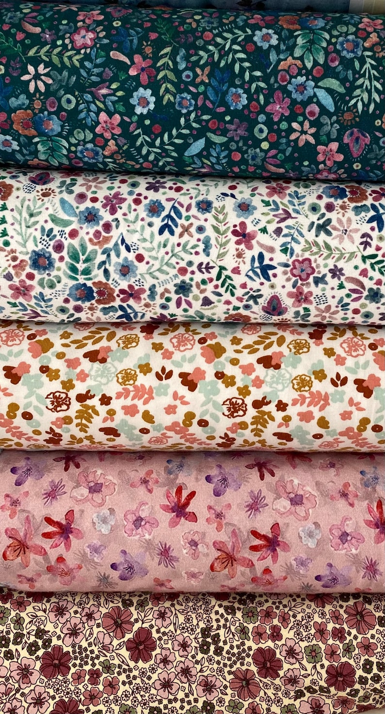 May include: Five different fabric swatches with floral patterns. The top swatch is a dark teal fabric with a small floral pattern. The second swatch is a white fabric with a small floral pattern. The third swatch is a light pink fabric with a small floral pattern. The fourth swatch is a light pink fabric with a larger floral pattern. The bottom swatch is a light beige fabric with a small floral pattern.