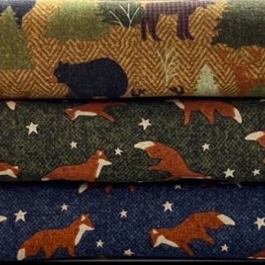 May include: Three rolls of fabric with woodland animal patterns. The top roll has a brown and gold herringbone pattern with deer, bears, and trees. The middle roll is green with foxes and stars. The bottom roll is blue with foxes and stars.