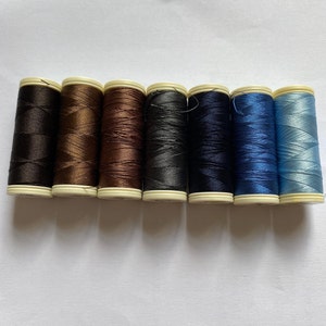 May include: Eight spools of thread in various colours, including black, brown, dark grey, navy blue, and light blue. The spools are arranged in a row from left to right.