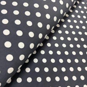 May include: Dark navy fabric featuring a repeating pattern of large white polka dots. The fabric is folded, revealing its texture and drape. Suitable for sewing, the material has a classic and versatile design, perfect for various projects.