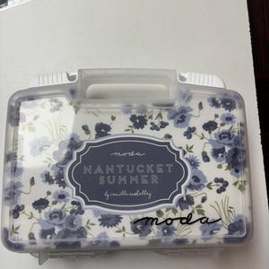 May include: Clear plastic storage case with a floral pattern in shades of blue. The case has a white handle and the words "Nantucket Summer" are printed on the front.
