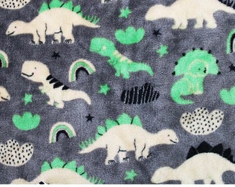 Può includere: Un tessuto grigio con un motivo ripetuto di dinosauri bianchi e verdi, stelle e arcobaleni.