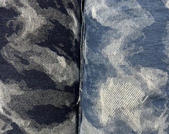 Può includere: Due rotoli di tessuto con motivo mimetico. Il rotolo a sinistra presenta una combinazione di colori blu navy scuro e bianco, mentre quello a destra mostra una tonalità di blu più chiara e bianco. Entrambi i tessuti hanno una trama visibile.