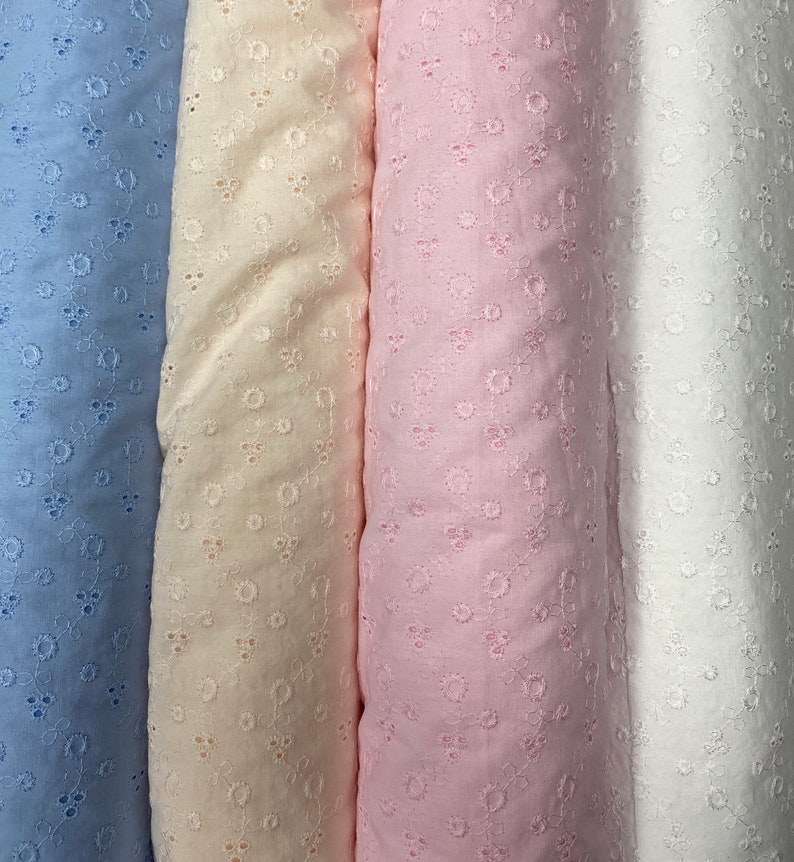 May include: Four rolls of fabric with a delicate eyelet pattern. The fabric is in shades of light blue, cream, pink, and white.