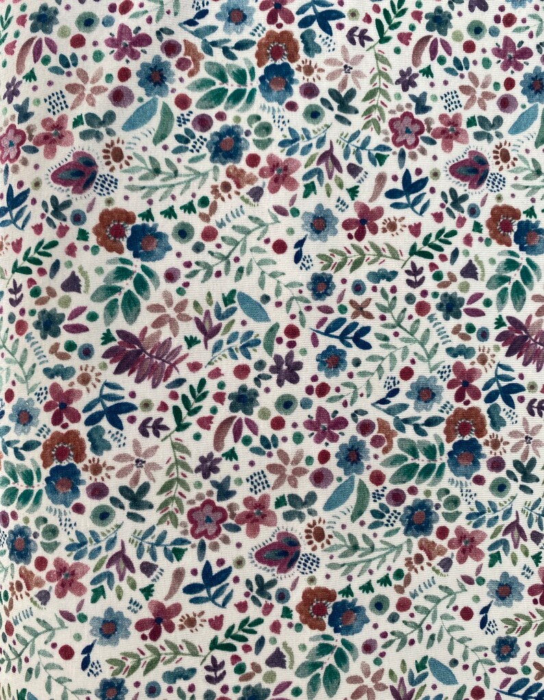 May include: A white fabric with a repeating pattern of small, colorful flowers and leaves. The flowers are in shades of pink, red, blue, and green.