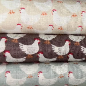 Puede incluir: Tres muestras de tela con un patr&oacute;n repetitivo de pollos blancos sobre fondos de diferentes colores. La muestra superior es beige, la muestra del medio es marr&oacute;n y la muestra inferior es azul claro.