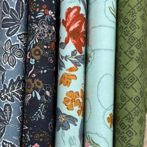 May include: Close-up of several fabric rolls with floral patterns. The fabrics feature various designs, including leaves, flowers, and geometric shapes, in shades of blue, navy, orange, and green. The rolls are tightly wound, showcasing the detailed patterns.