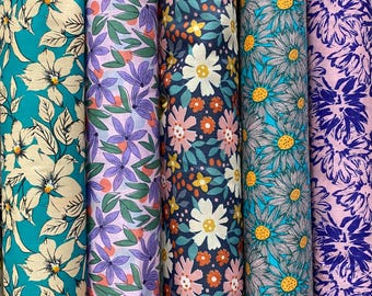 Può includere: Una collezione di rotoli di tessuto a fantasia floreale. I disegni includono grandi fiori color crema su turchese, fiori viola con foglie verdi, fiori rosa e bianchi su blu navy, margherite turchesi e motivi floreali viola.