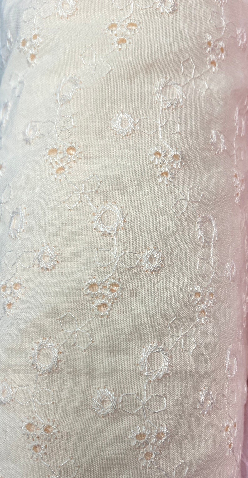 May include: White fabric with a delicate embroidered floral pattern. The fabric has a subtle texture and a soft, airy feel.