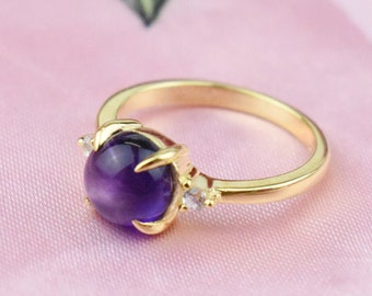 May include: A gold ring with a large, round, purple amethyst gemstone surrounded by smaller clear gemstones.