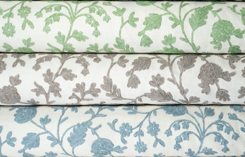 May include: Three fabric rolls with a white background and a floral pattern. The top roll has green flowers, the middle roll has gray flowers, and the bottom roll has blue flowers.