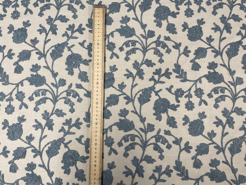 May include: A close-up of a fabric with a blue floral pattern on a white background. A ruler is placed next to the fabric to show the scale.