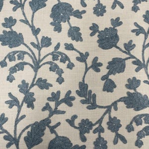 May include: A cream-colored fabric with a blue embroidered floral pattern. The design features delicate branches with small flowers and leaves.