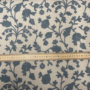 May include: Blue floral embroidery on a cream-colored fabric. A wooden ruler is placed on the fabric for scale.