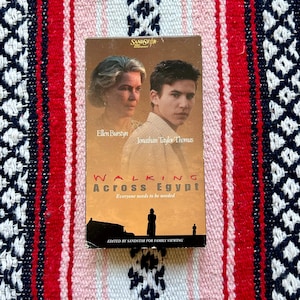 May include: A VHS tape of the film Walking Across Egypt featuring Ellen Burstyn and Jonathan Taylor Thomas on the cover. The brown cover includes the Sandstar Entertainment logo, the title, and the tagline Everyone needs to be needed.