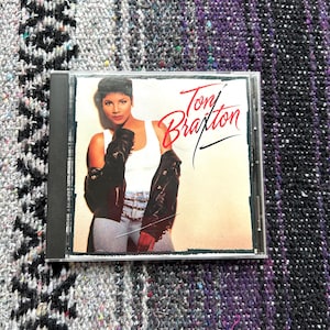 May include: A CD case with a photo of Toni Braxton on the front. She is wearing a white tank top, a black leather jacket, and blue jeans. The title of the album is "Toni Braxton" in black and red lettering.