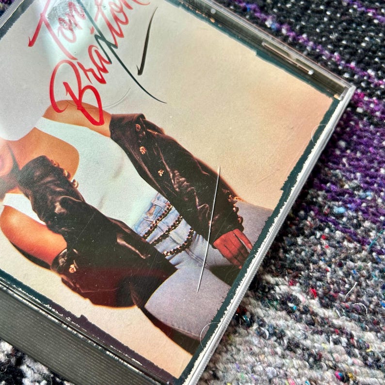 May include: A compact disc case with a photo of a woman wearing a white shirt and a black leather jacket. The title "Toni Braxton" is written in red on the front of the case.