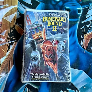 May include: VHS video cassette cover for the film Homeward Bound II: Lost in San Francisco. The cover features a colourful illustration of a cat, a dog, and a golden retriever running down a street in San Francisco. The text on the cover reads "WALT DISNEY PICTURES PRESENTS HOMEWARD BOUND II Lost in San Francisco" and "Totally Irresistible... A Family Winner!"