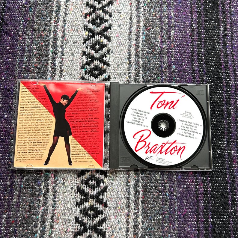May include: A CD case with a red, white, and black cover featuring a woman in a black dress. The CD case includes a CD with a black and white image of Toni Braxton and the title "Toni Braxton".
