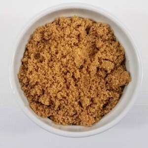 May include: A white bowl filled with brown sugar.