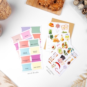 K&ouml;nnte beinhalten: Ein Set aus 24 farbigen K&uuml;chenetiketten mit Kategorien wie "Fleisch", "Salate" und "Desserts". Au&szlig;erdem ein Set kulinarischer Aufkleber mit Lebensmittelillustrationen, darunter ein K&uuml;rbis, eine Avocado und Honig. Die Etiketten und Aufkleber liegen auf einer wei&szlig;en Oberfl&auml;che.